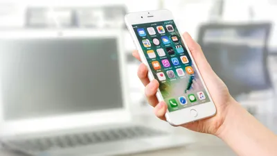 Айфон в руке на фоне ноутбука, фото - Новости Zakon.kz от 02.05.2025 17:26